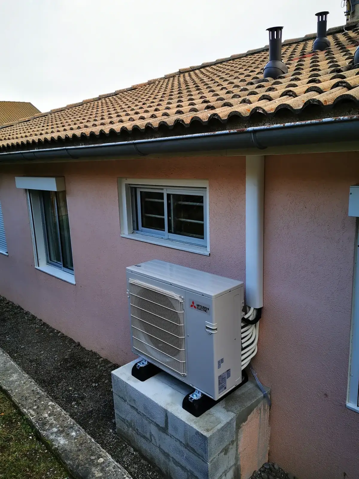 Groupe extérieur de climatisation multi-split Mitsubishi Electric posé sur des parpaings contre une façade, à Corenc, installé par Air Eco Clim